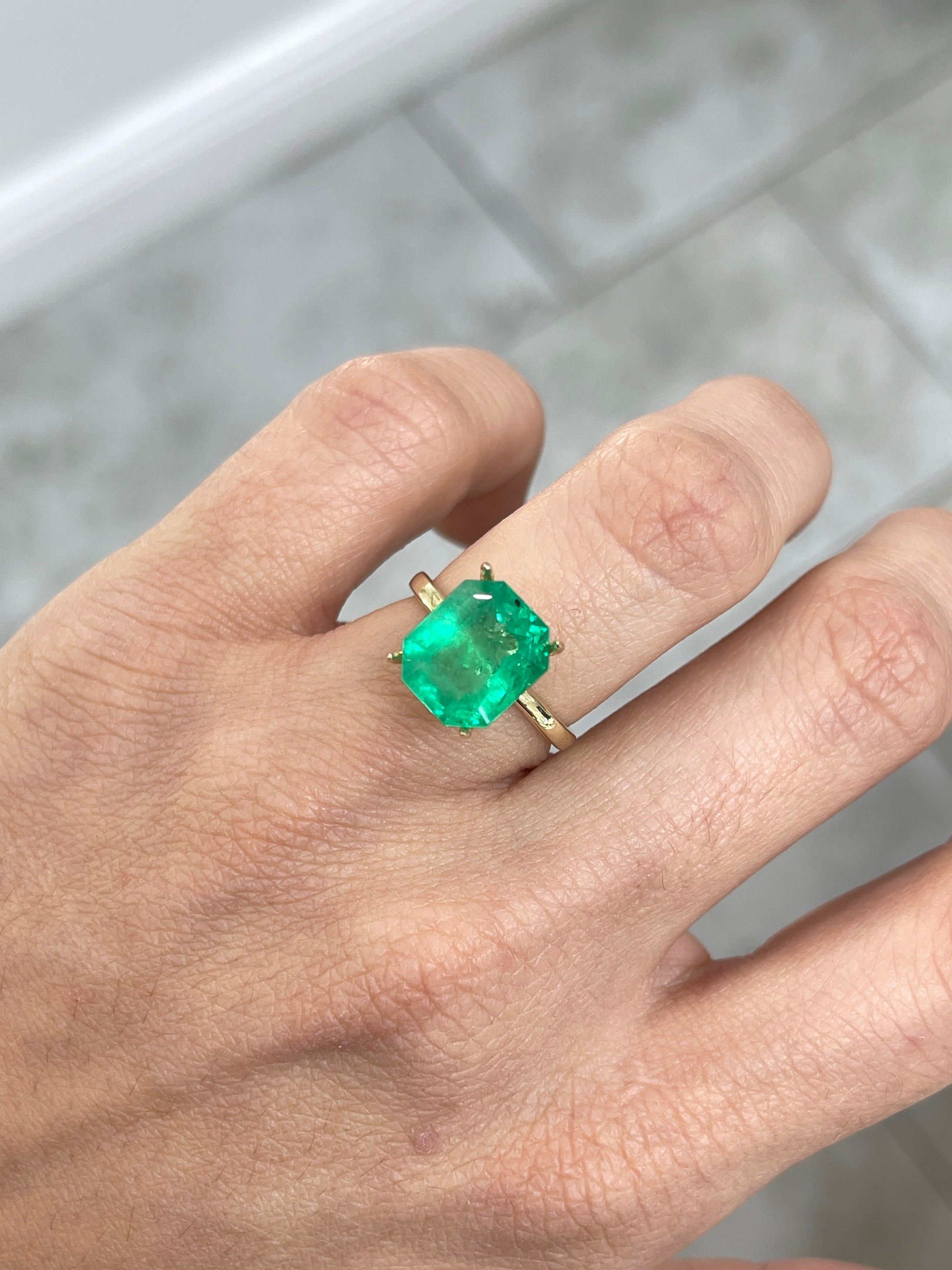 Natural 5.75 carat medium green Colombian emerald loose gemstone in emerald cut, showing freckled surface and vibrant color.