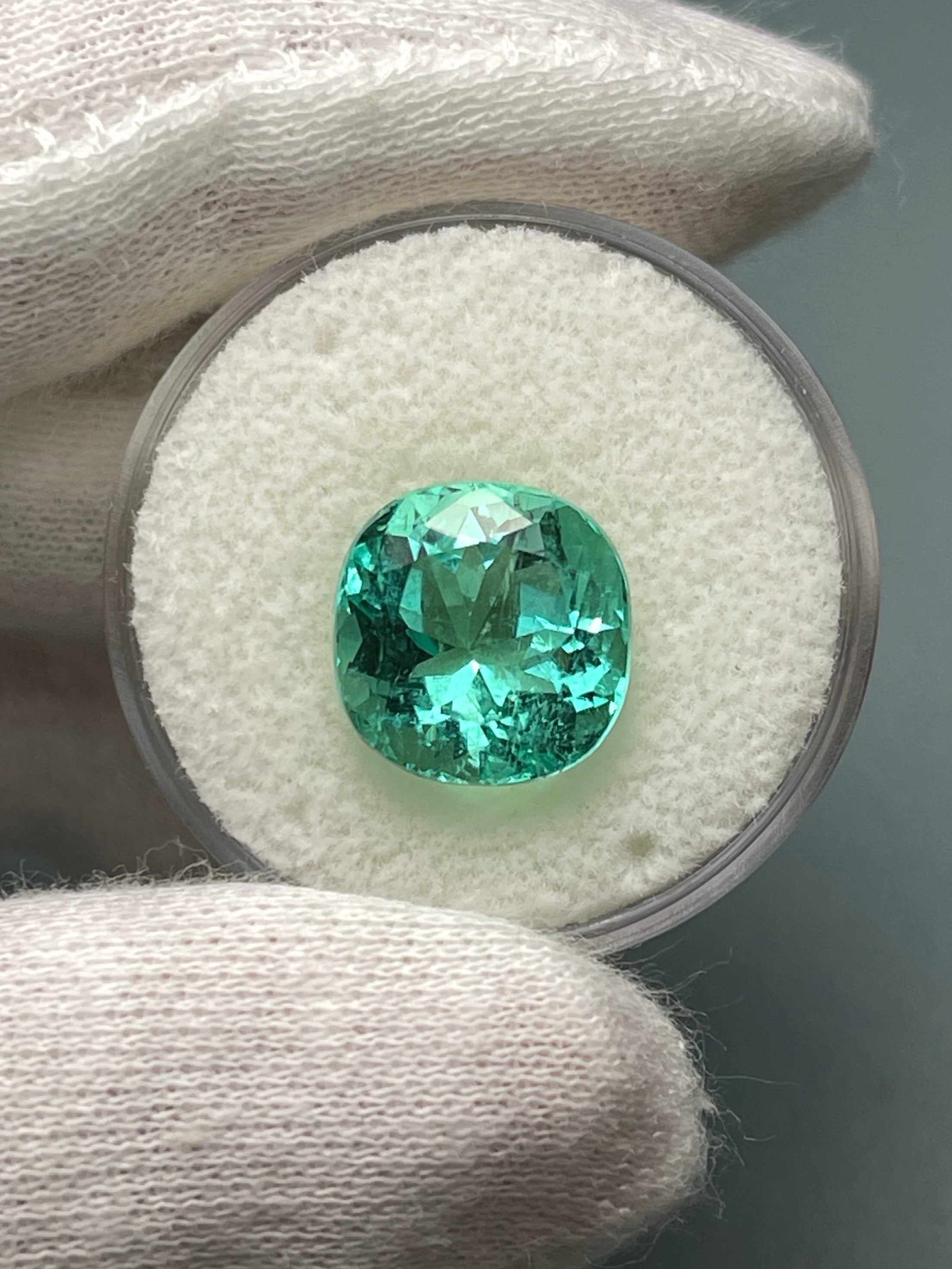 Luminous bluish-green 6.38 carat cushion cut Colombian emerald natural loose gemstone, displayed on a neutral background.