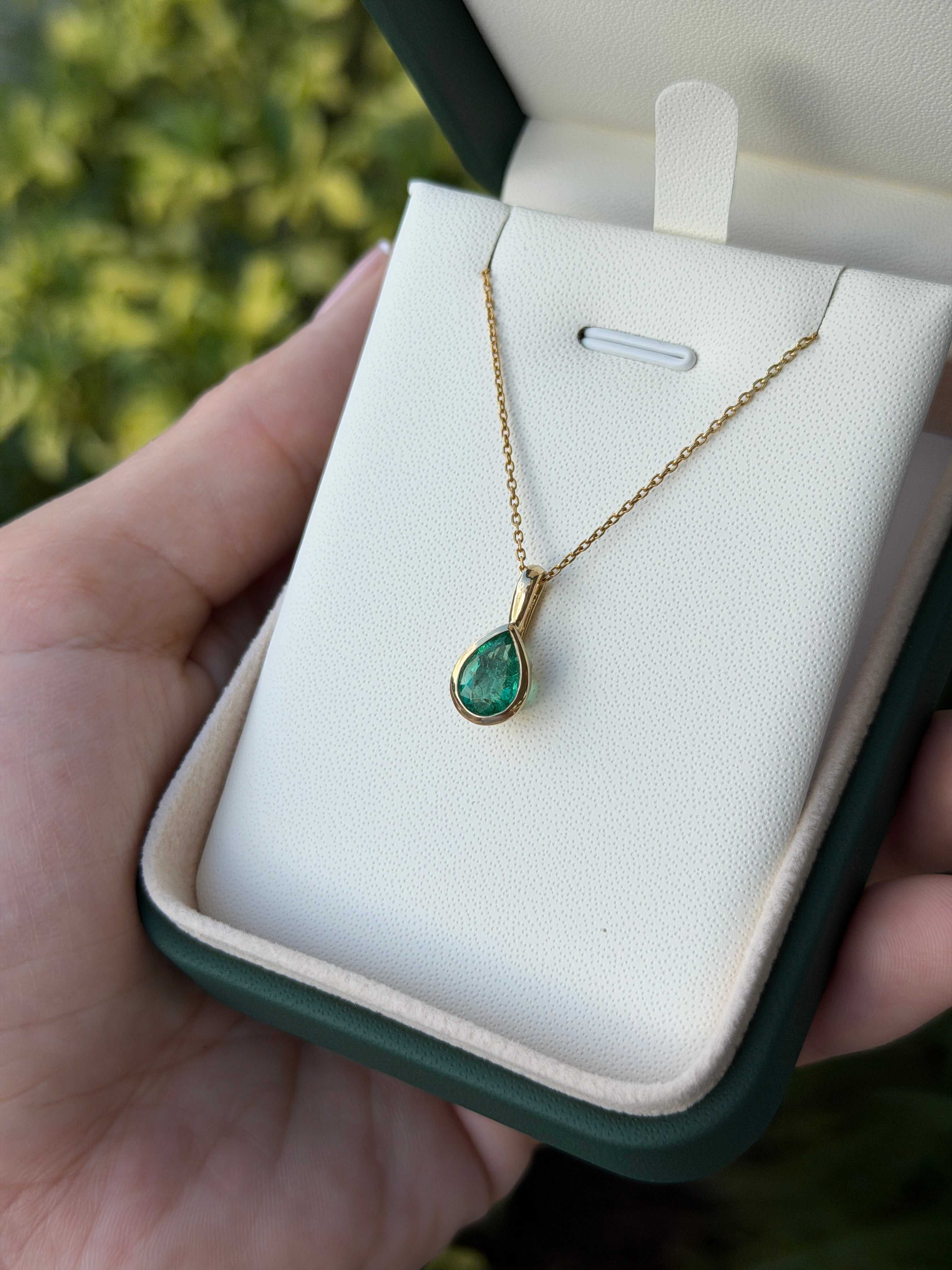 Helena 1.0ct bezel set natural emerald pear pendant necklace in 14K gold, from JR Colombian Emeralds, with a detailed close-up view.