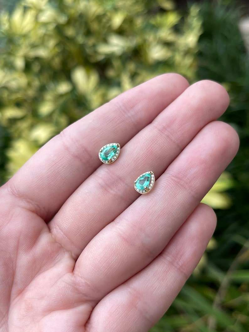 Natural emerald and diamond halo pear cut earrings in 14K gold, featuring Colombian emeralds and intricate design detail.