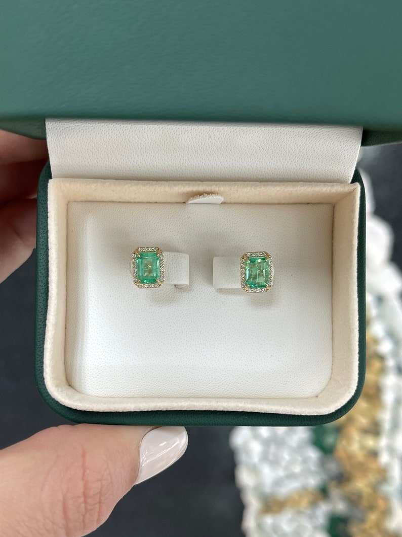Colombian Emerald 14K gold stud earrings with 2.10 carat total weight, natural emerald-cut diamonds, and halo design.