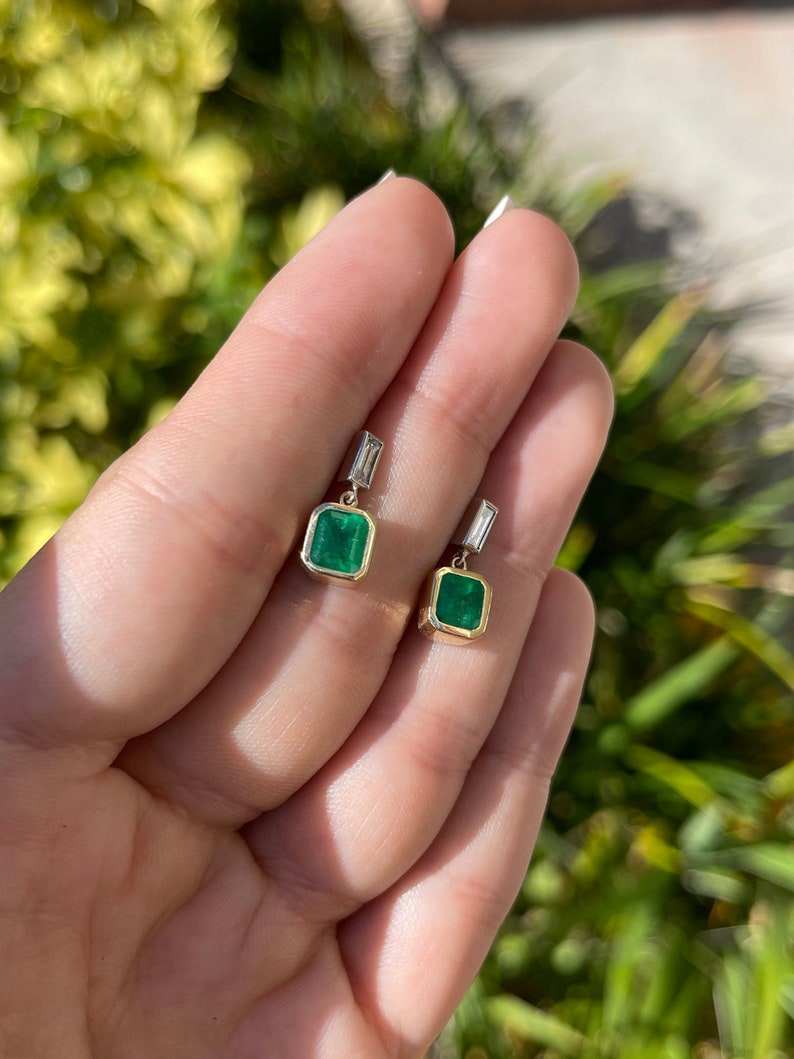 Deep green emerald and diamond dangle bezel earrings in 14K gold featuring Colombian emeralds and sparkling accents.