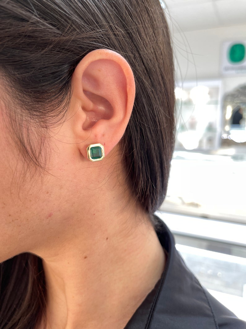 Colombian Emerald 14K yellow gold bezel stud earrings featuring dark vivid green top emeralds, close-up of the elegant jewelry.