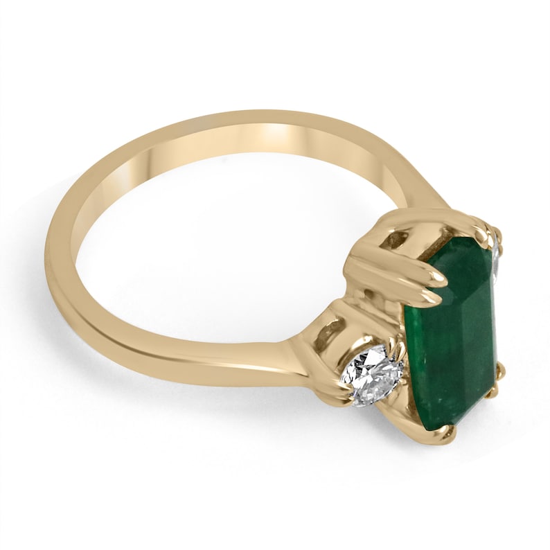 Colombian Emerald 18K gold three-stone engagement ring featuring a deep dark alpine green emerald cut and round diamonds.