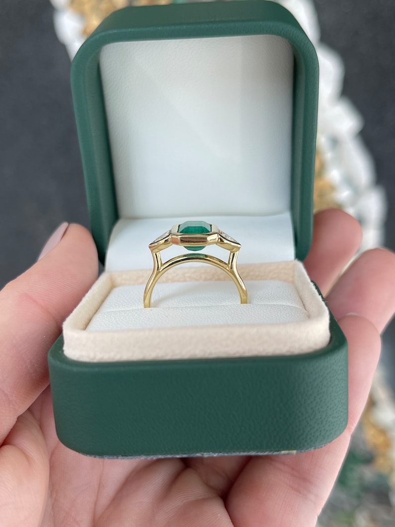 Colombian Emerald and heart cut diamond three-stone engagement ring in 18K yellow gold with dark alpine hue and 2.97tcw total weight.