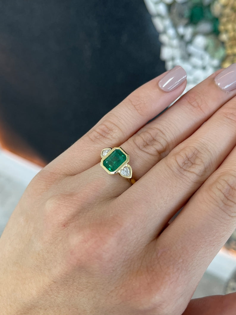 Colombian Emerald 18K yellow gold engagement ring with 2.97tcw emerald and heart-cut diamonds, three-stone design.