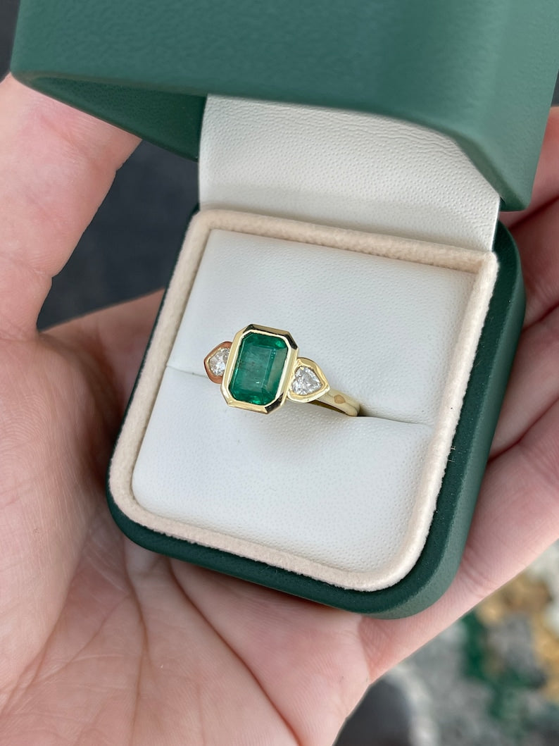 Emerald and heart cut diamond three-stone engagement ring with 18K yellow gold and Colombian emerald accents.