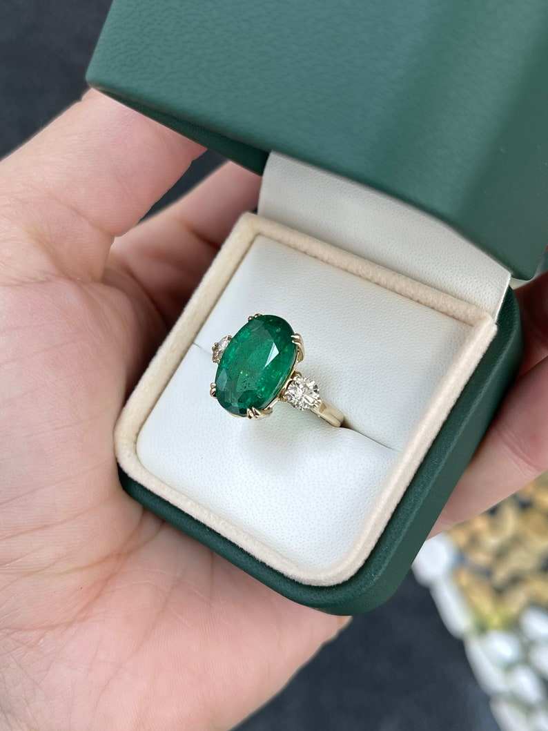 Dark green oval emerald and round diamonds on 14K Colombian Emerald engagement ring with double prong setting.