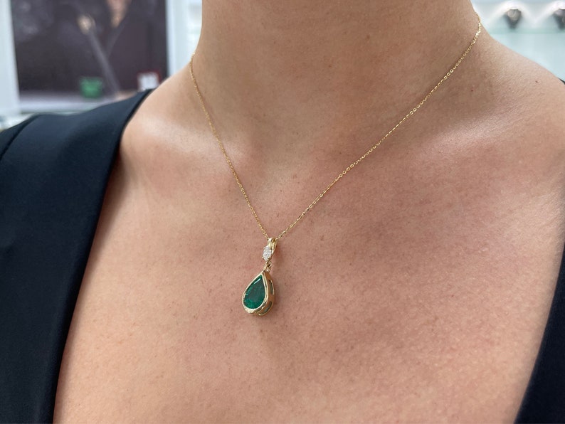 Emerald pendant necklace featuring a pear-cut emerald with marquise diamond accents in 14K gold bezel setting.