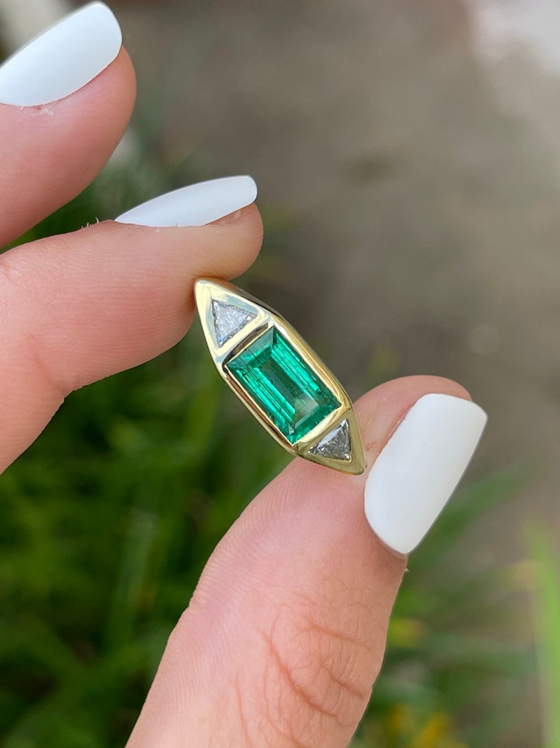 Ladies emerald ring featuring 2.35cttw three stone design with baguette, vivid emeralds, and trillion cut diamonds in 18K gold.
