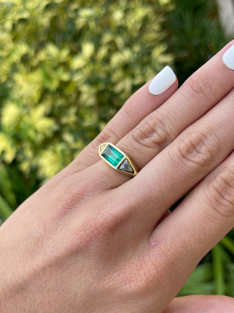 Ladies emerald ring featuring three-stone design with vivid emerald and trillion cut diamonds in 18K gold by Colombian Emerald.
