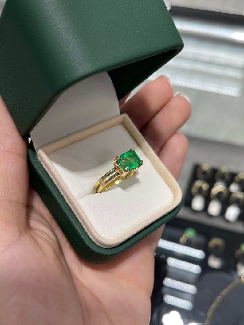Emerald cut yellowish-green Colombian emerald ring with double claw prong, 18K gold split shank design for ladies.