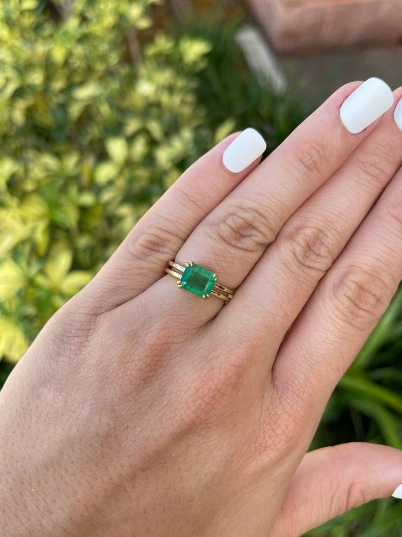 Ladies emerald ring featuring a 2.68ct Colombian emerald cut east-west yellowish-green gemstone with double claw prongs in 18K gold.