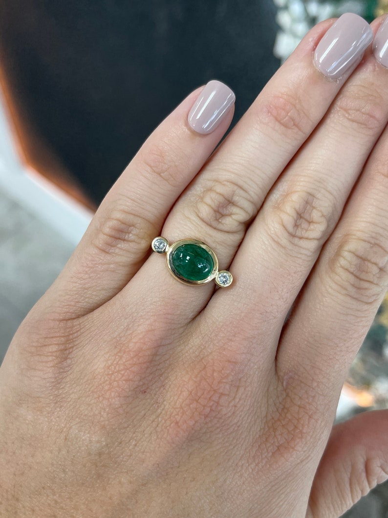 Ladies emerald ring featuring a 4.50tcw oval dark green emerald cabochon with diamond accents in a 14K setting.