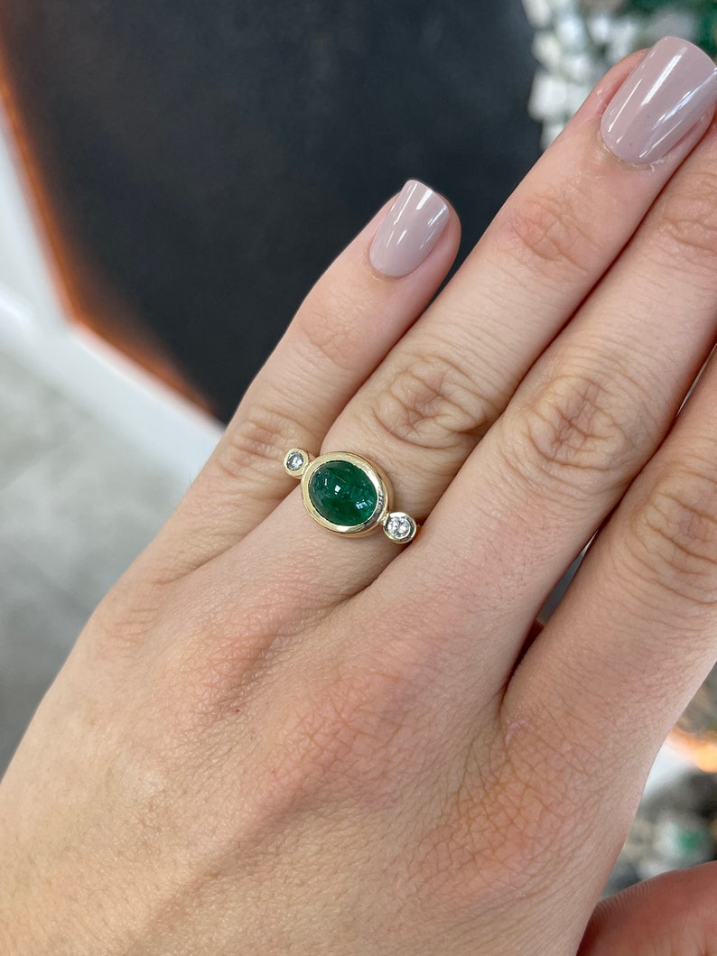 Ladies emerald ring featuring a 4.50tcw oval-shaped dark green emerald cabochon with diamond accents in 14K gold.