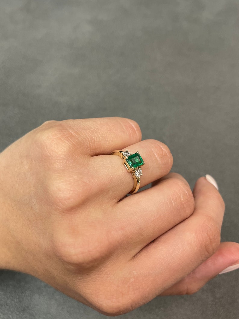 14K gold Colombian Emerald three-stone ring with brilliant round diamonds, showcasing a transparent design and elegant craftsmanship.