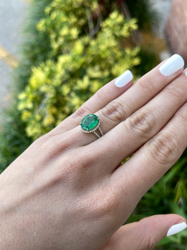 14K Colombian Emerald and diamond halo engagement ring with oval emerald center and split shank design.