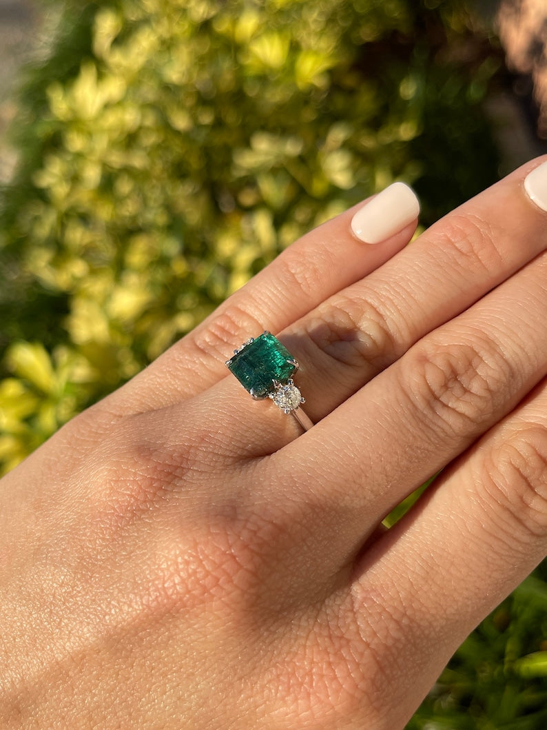 14K gold 4.90tcw dark green emerald and diamond 3-stone engagement ring with Asscher cut emerald and round diamonds.