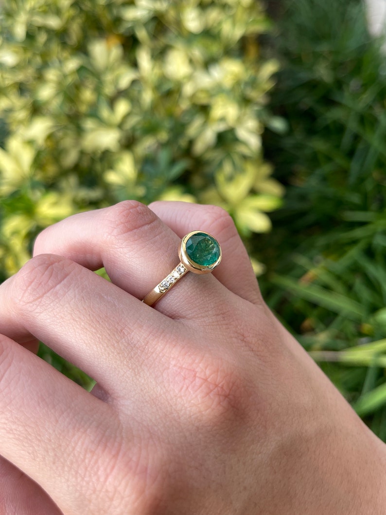 18K gold ring with 5.66tcw oval cut dark green emerald and diamond accents, bezel setting, Colombian Emerald brand.