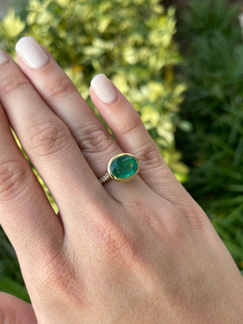 18K gold ring with 5.66ctw dark green oval cut emerald and diamond accents, bezel setting, Colombian Emerald brand.