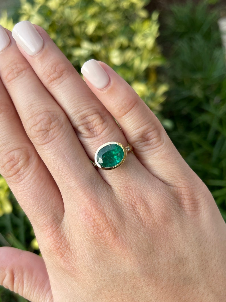 18K gold ring with a dark green oval cut emerald and diamond accents in a bezel setting, Colombian Emerald brand.