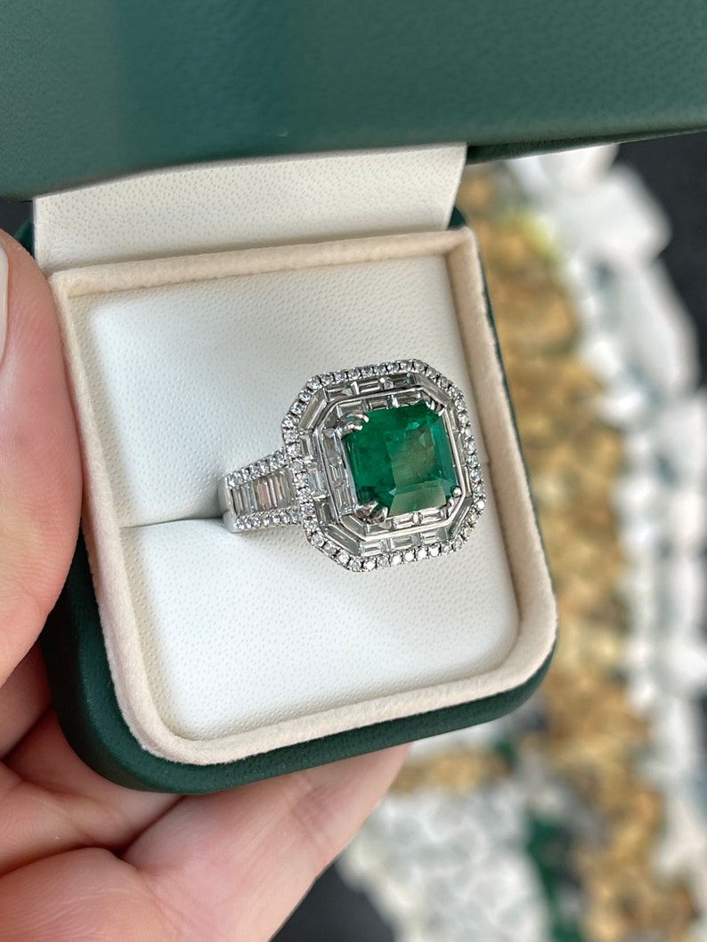 Colombian Emerald 18K white gold statement ring with emerald and diamond halo, triple diamond accents, and intricate design.