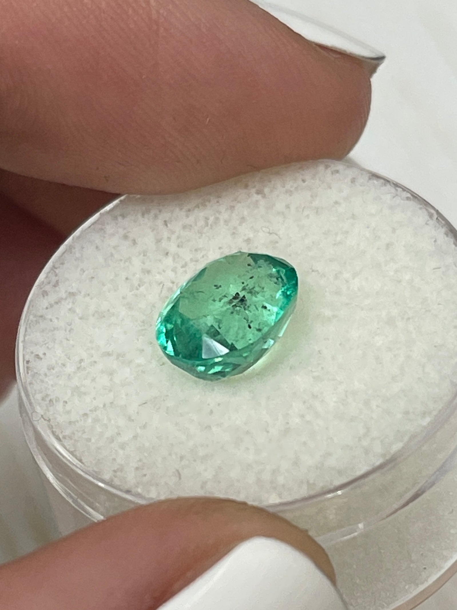 Vibrant 2.83-carat natural Colombian emerald loose oval cut with green color and natural freckles, displayed on a white background.