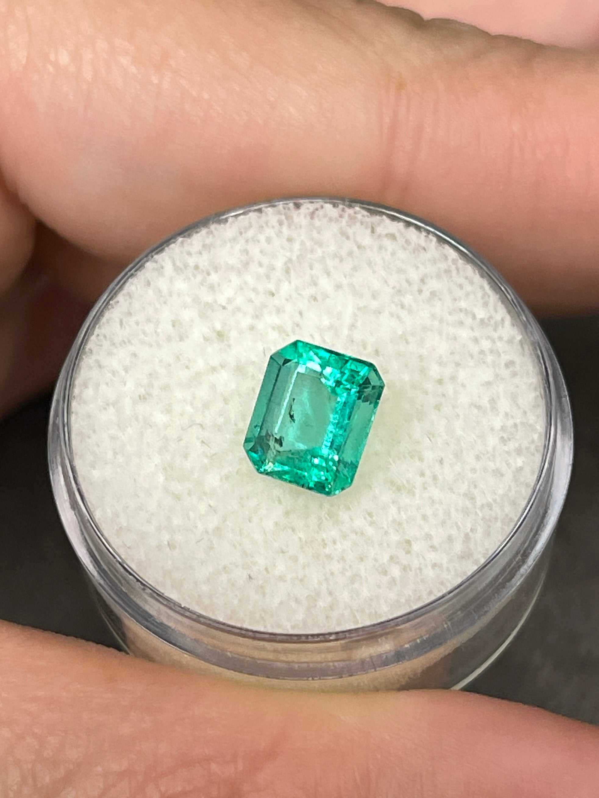Bright bluish green 1.69 carat Colombian emerald loose gemstone in an emerald cut, displayed with a gold ring setting.