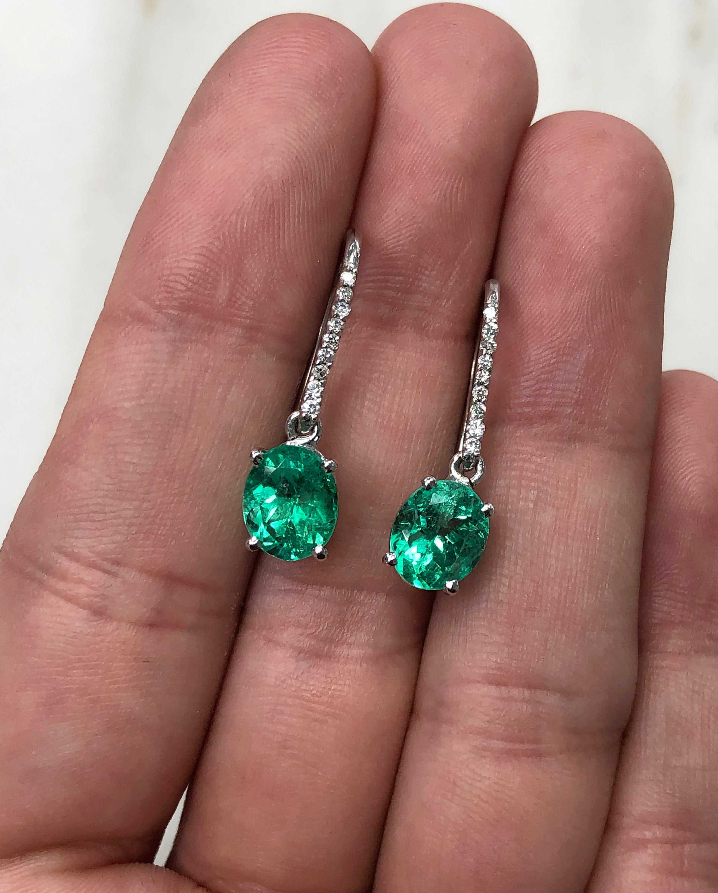 Fine quality vivid green Colombian emerald oval and diamond dangle earrings in 14K gold, featuring luxurious gemstone accents.
