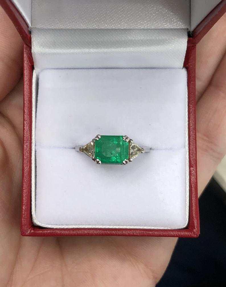 Three-stone emerald cut Colombian and trillion diamond engagement ring by JR Colombian Emeralds, 18K gold, showcasing east-to-west design.