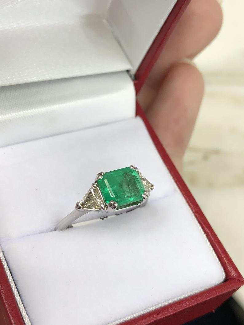Three-stone engagement ring with emerald-cut Colombian emeralds and trillion diamonds in 18K gold by JR Colombian Emeralds.